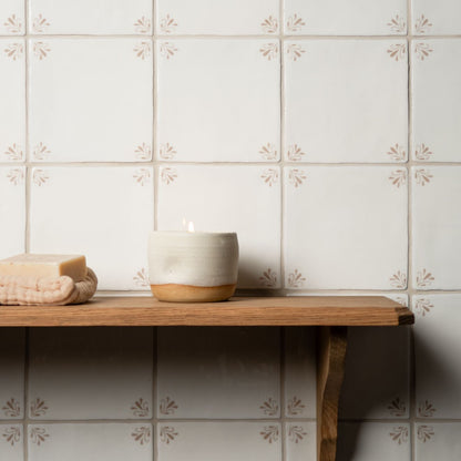 Candle and soap on a wooden shelf against a tiled wall