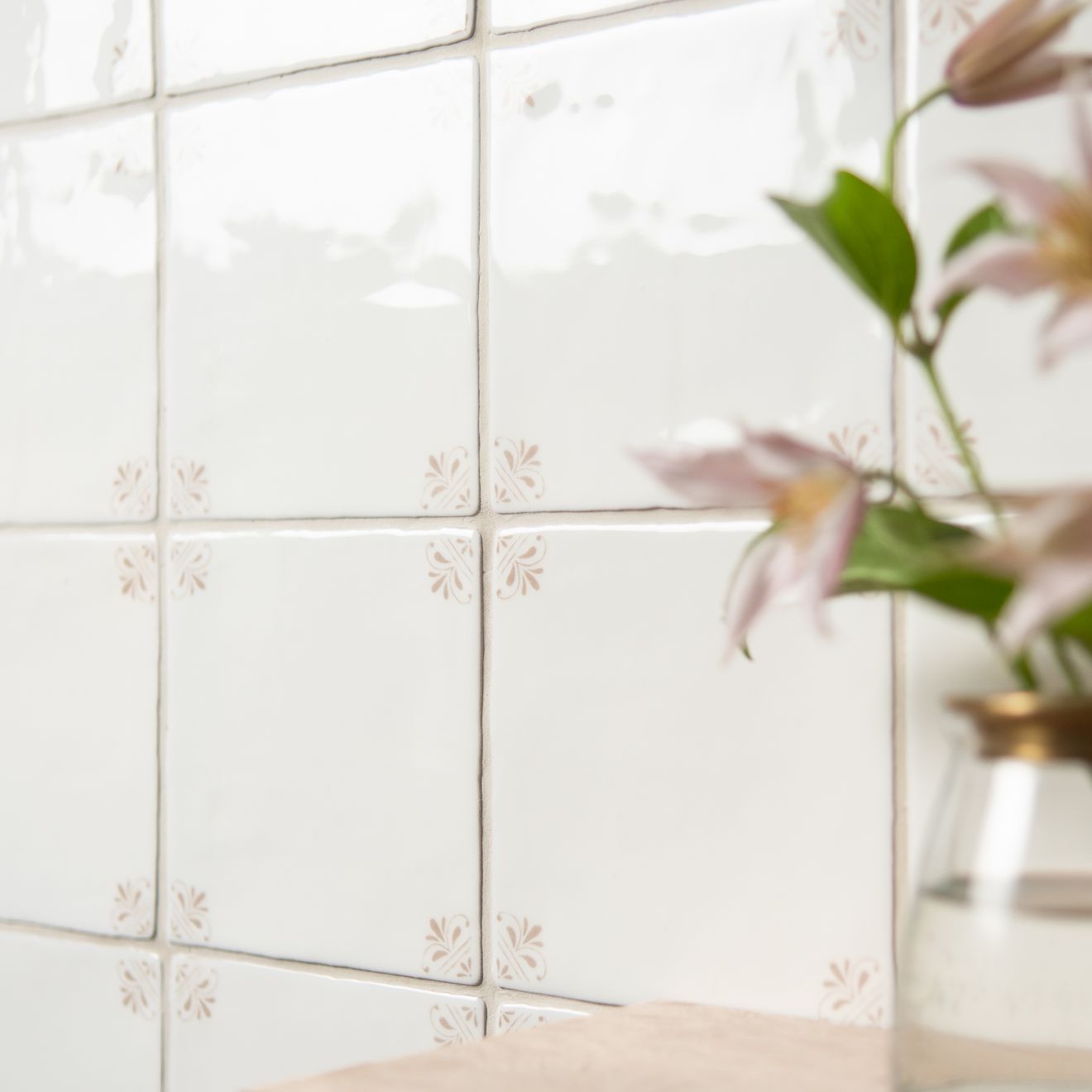 White tiled wall with decorative cutouts and a vase with flowers in the corner.