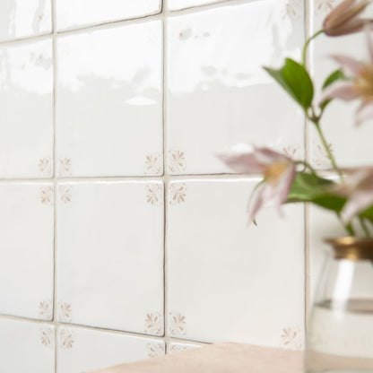 White tiled wall with decorative cutouts and a vase with flowers in the corner.