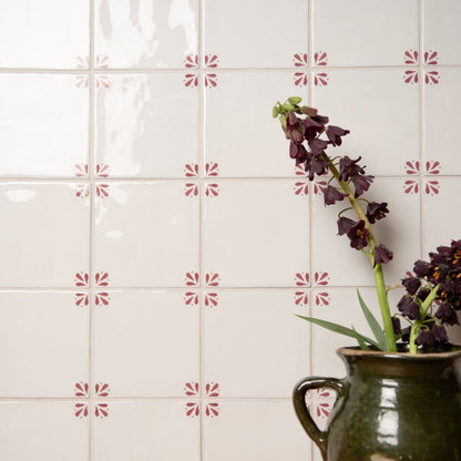 Decorative tiles with a floral pattern on a white wall with a vase of flowers.