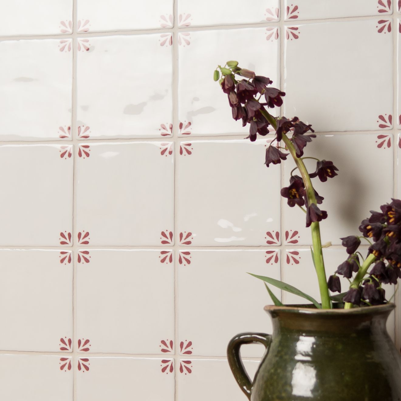 Brown ceramic pitcher with purple flowers against a tiled wall with decorative pink patterns