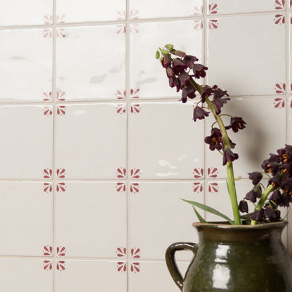Brown ceramic pitcher with purple flowers against a tiled wall with decorative pink patterns