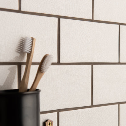 Two bamboo toothbrushes with white bristles in a matte black holder displayed with crackle glazed brick tile helmingham