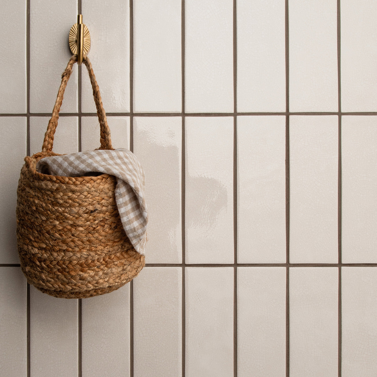 A woven jute basket with braided handles holding a gray and white checkered cloth for storing crackle glazed brick tile helmingham