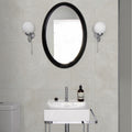 Black oval mirror with sleek modern frame mounted above dorset porcelain white ceramic sink in bathroom setting