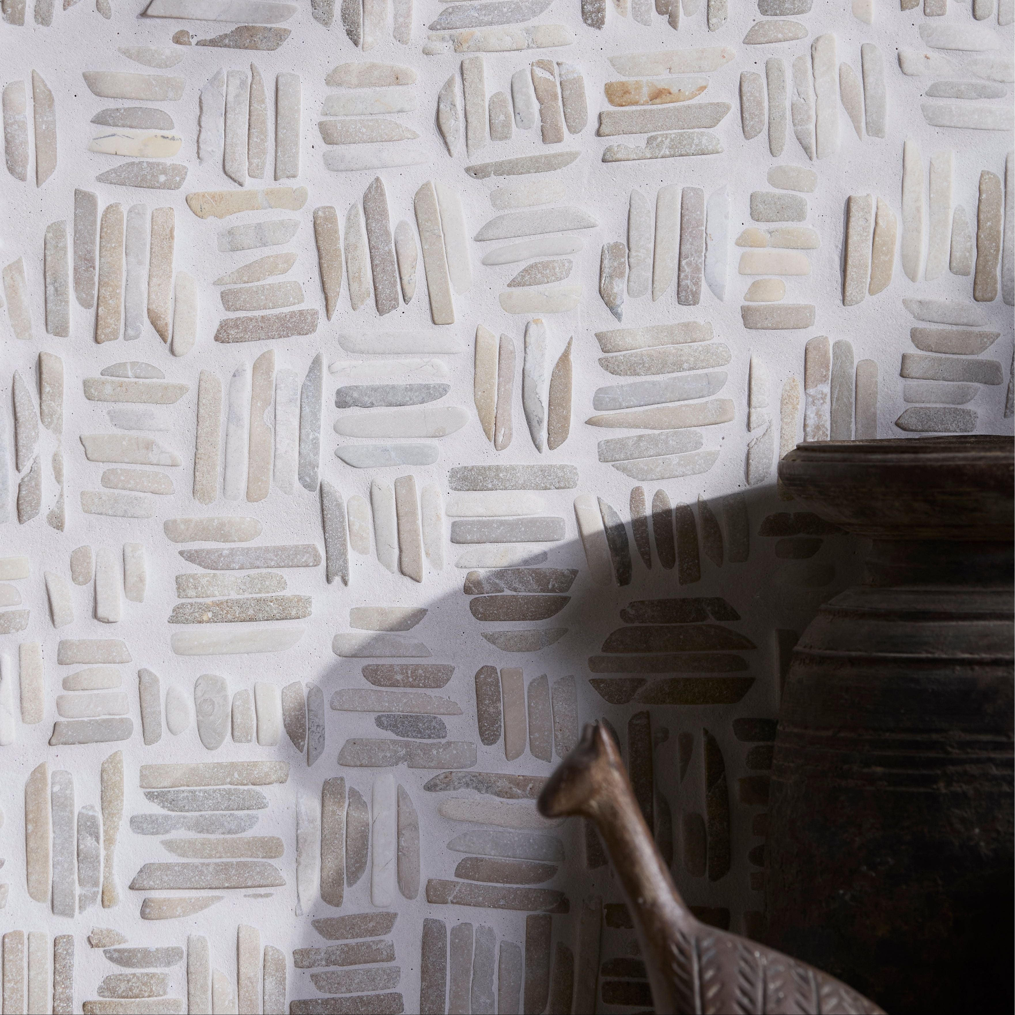 Decorative wall on Enso Organic Basketweave Limestone Mosaic Tiles with geometric pattern and a metallic object casting a shadow.