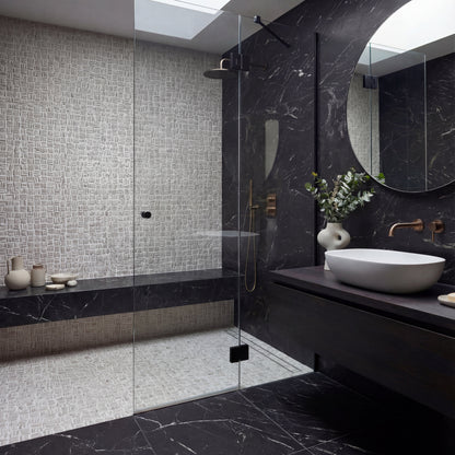 Modern bathroom with black marble walls, a glass shower enclosure, and a round mirror.