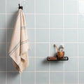 Beige towel hanging on a hook next to a small shelf with toiletries against a tiled wall.