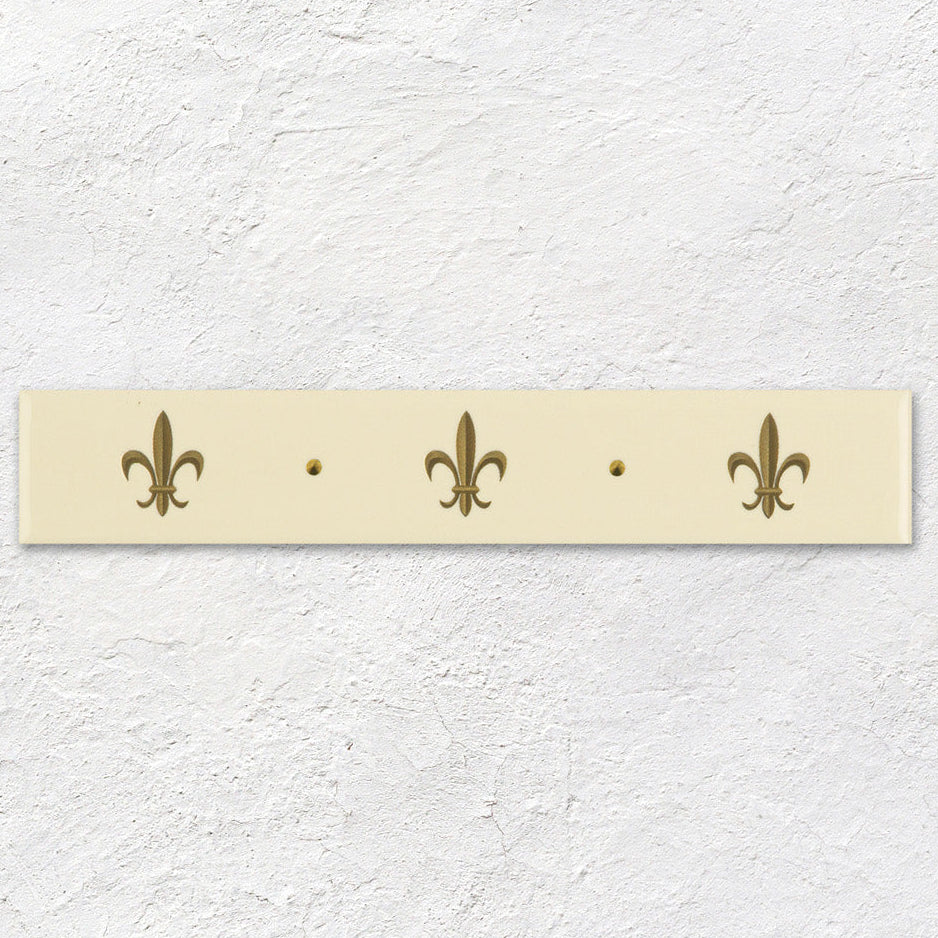 Cream-colored ceramic wall-mounted coat rack with three gold fleur de lis designs and two central mounting holes