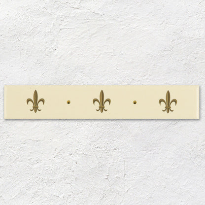Cream-colored ceramic wall-mounted coat rack with three gold fleur de lis designs and two central mounting holes