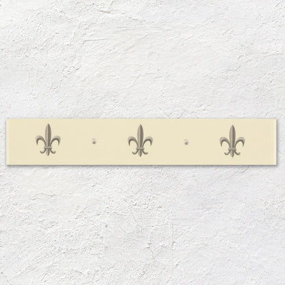Cream-colored rectangular wall-mounted coat rack with three metallic fleur de lis hooks in platinum on county white