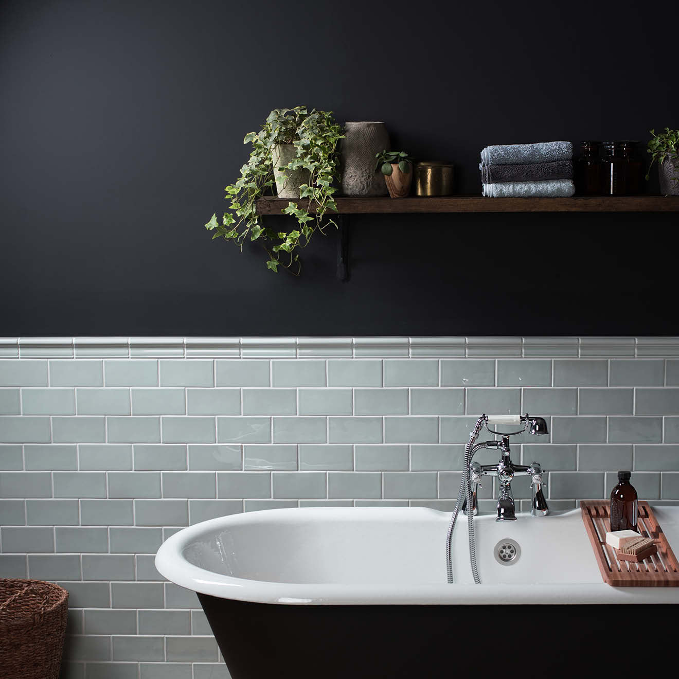 Bathroom with a black wall, white bathtub, and green tiles.