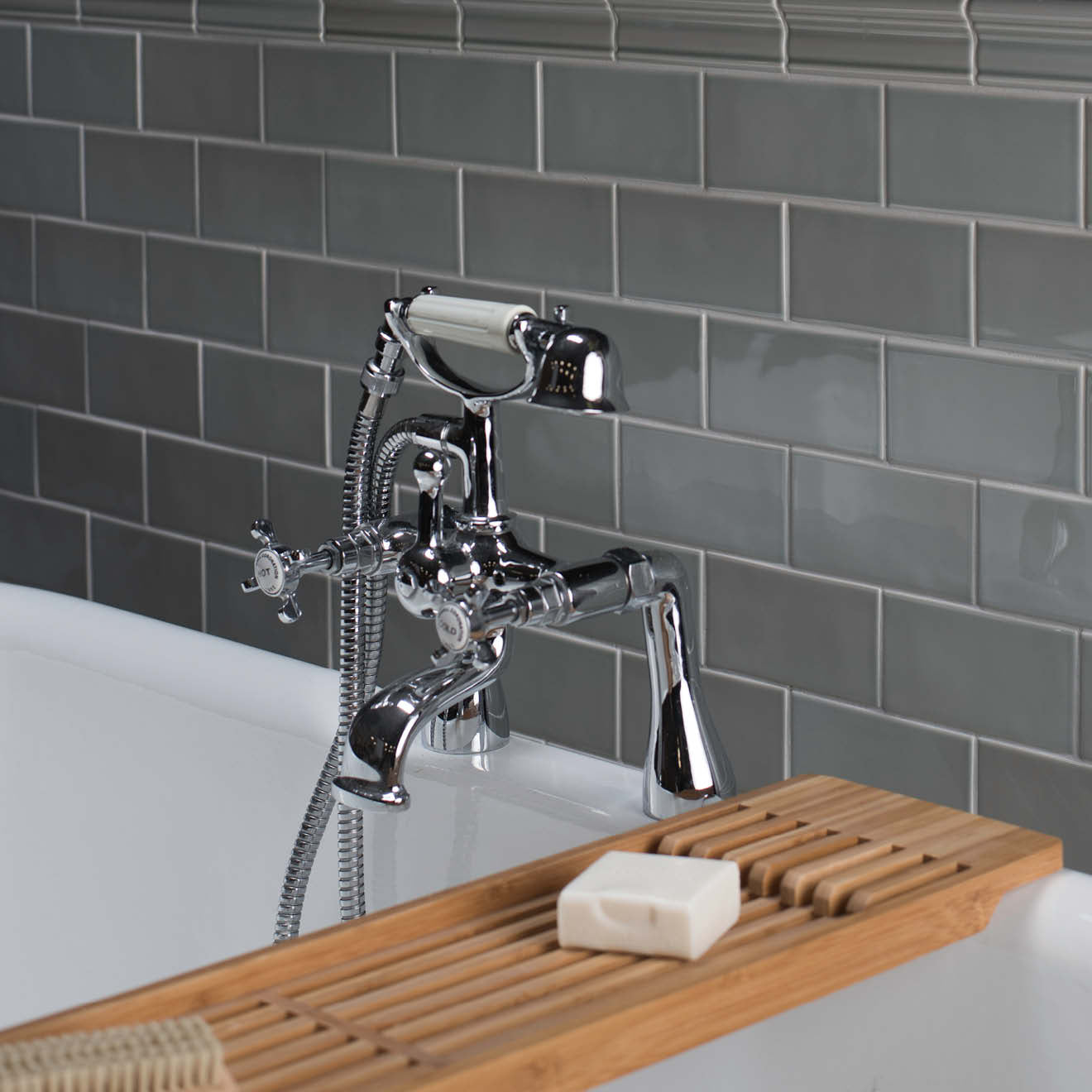 Chrome bathtub faucet with handheld shower head against a gray tiled wall.