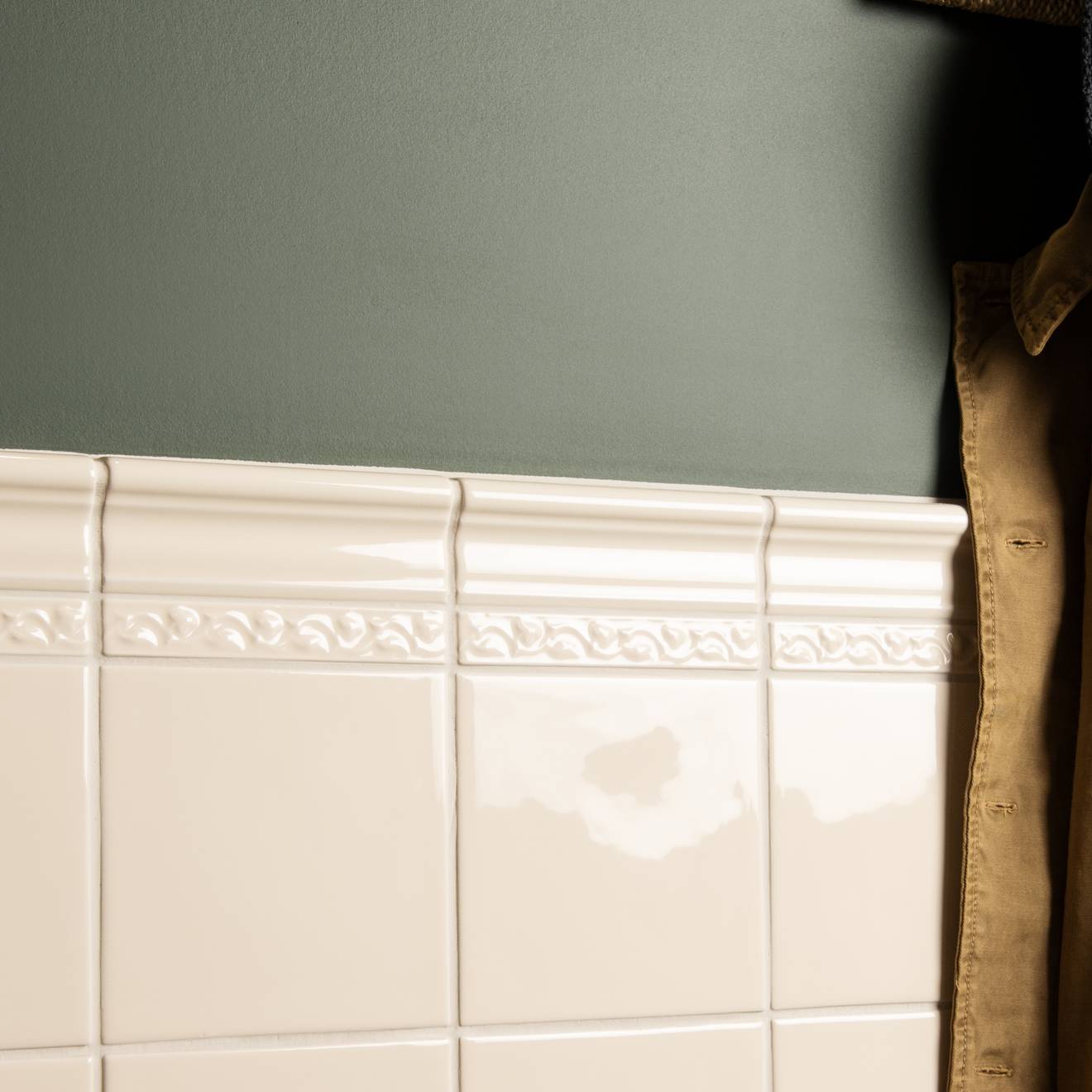 Close-up of a tiled wall with decorative border against a gray wall.