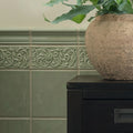 Decorative green tiles with intricate patterns and a textured vase on a black surface.