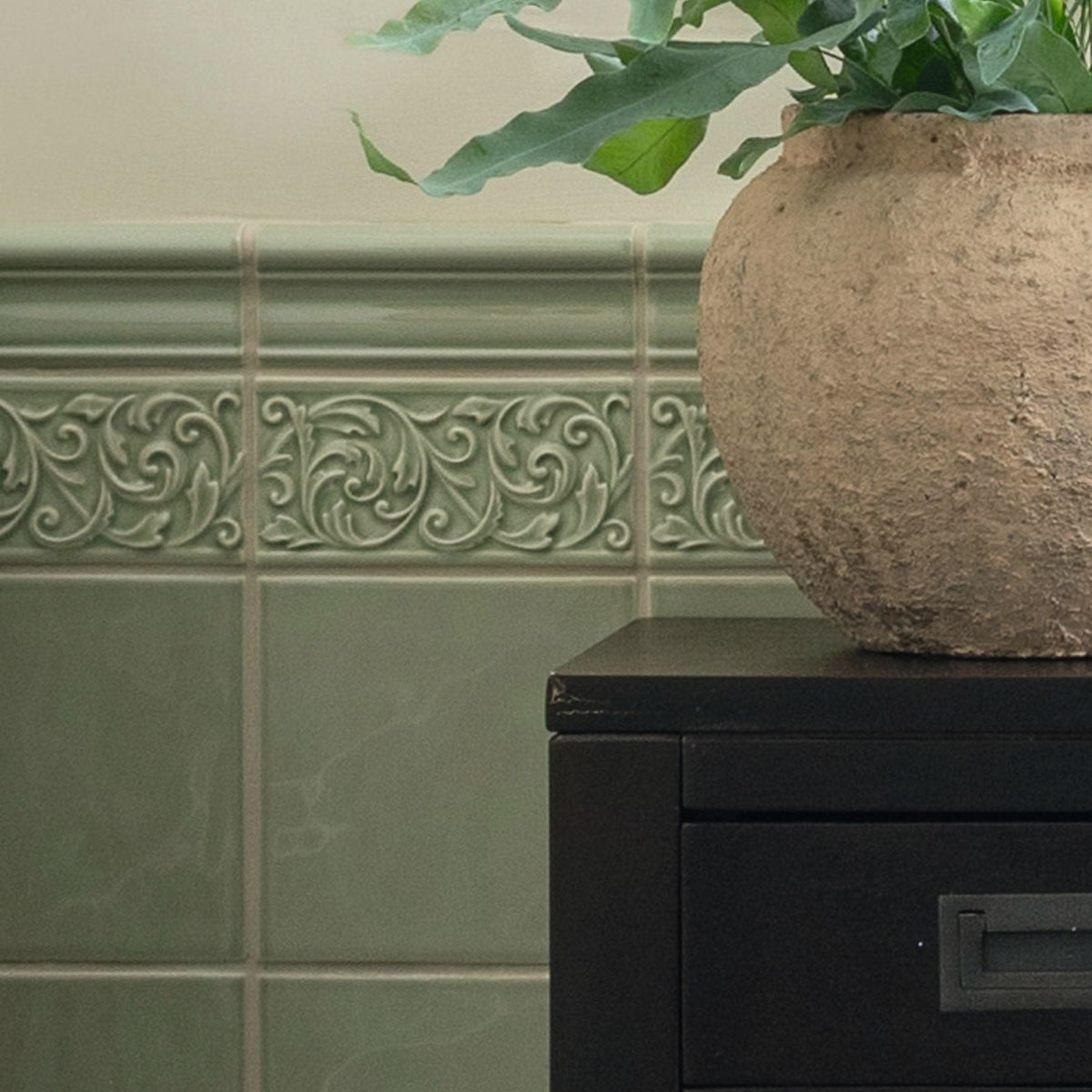 Decorative green tiles with intricate patterns and a textured vase on a black surface.