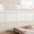 Decorative white tiles with intricate patterns on a beige tiled wall.