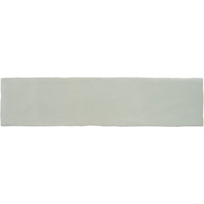A soft beige towel with white horizontal stripes and fringed edge hangs against muted gray large brick tile tern background