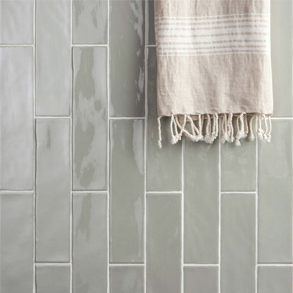 A soft beige towel with white horizontal stripes and fringed edges hanging against large brick tile tern gray backdrop