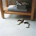 A pair of off-white minimalist slip-on sandals with smooth leather-like finish shown on moderna white porcelain 60 x 60 tile