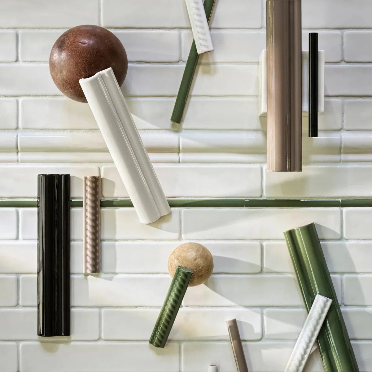 A styled flat-lay of decorative architectural molding pieces and textured rods arranged on a white subway tile background.