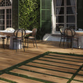 Outdoor dining area with tables and chairs on a wooden deck, greenery, and building in the background.