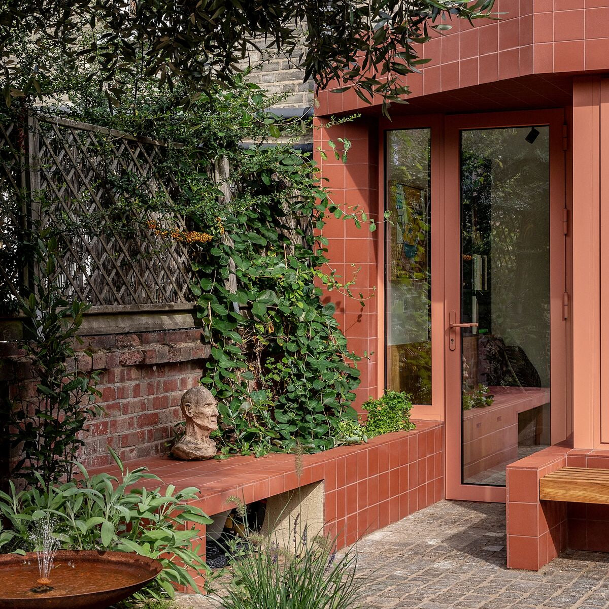Quarry red square tile terracotta tiled bench with weathered stone bust resting on its edge in outdoor setting