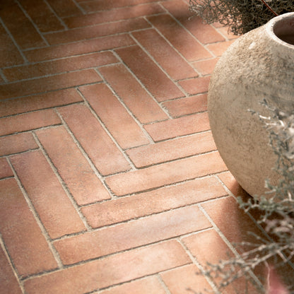 herringbone brick pavers arranged in a neat pattern, with a rustic beige stone planter partially visible on the right side.