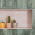 Three cacti in pastel ceramic pots yellow peach and beige on a pink tiled shelf featuring south cliff rose brick tile