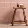 Wooden stool with a bottle and bowl against a pink tiled wall