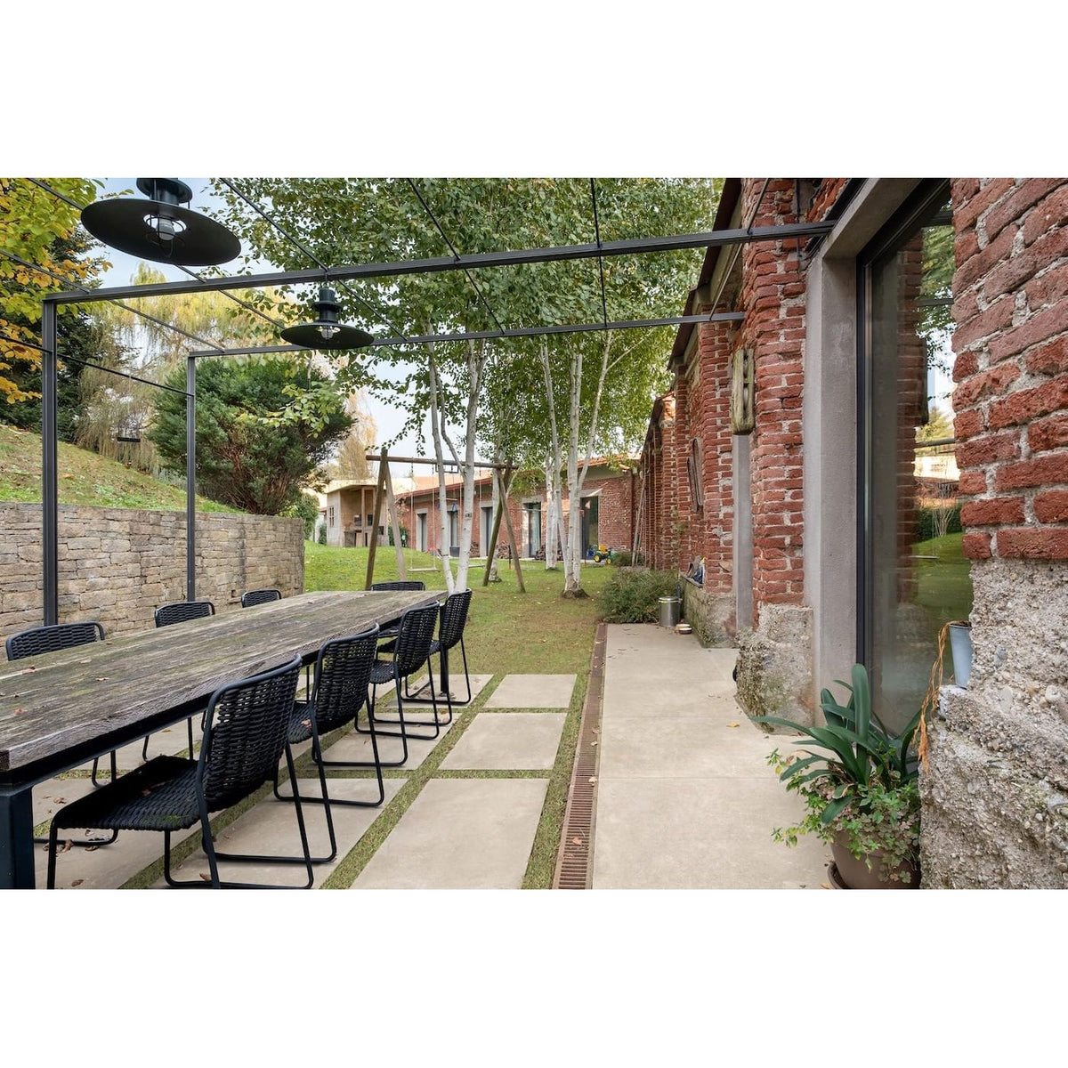 Outdoor dining area with long wooden table and chairs near a brick building.