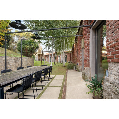 Outdoor dining area with long wooden table and chairs near a brick building.
