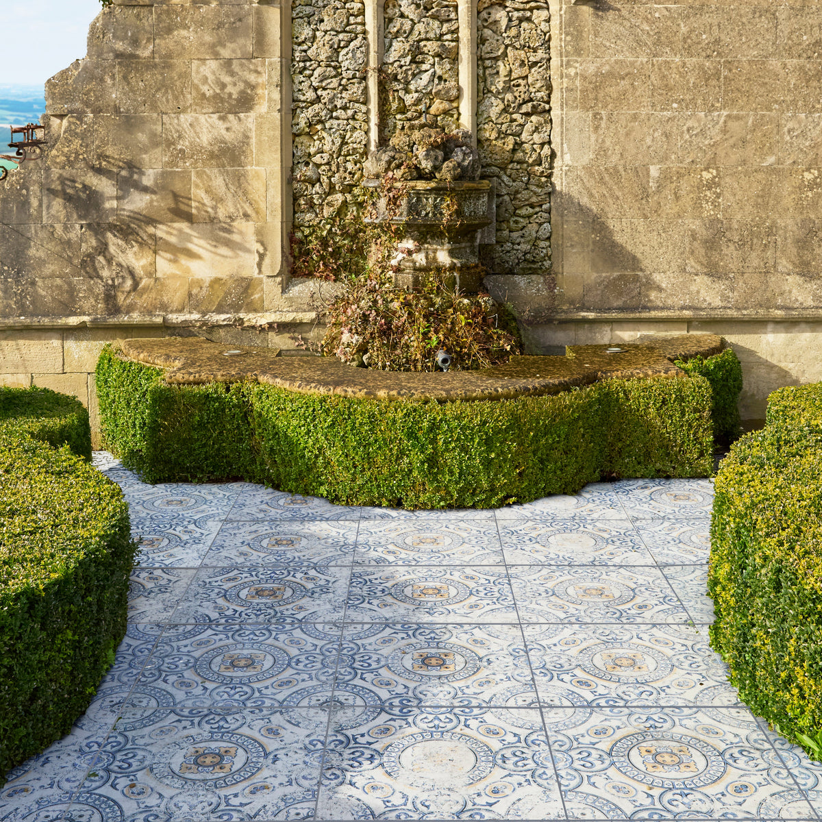 Decorative fountain in a garden with patterned tiles and stone wall.