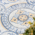 Decorative blue and white patterned tile with a blurred green plant in the background