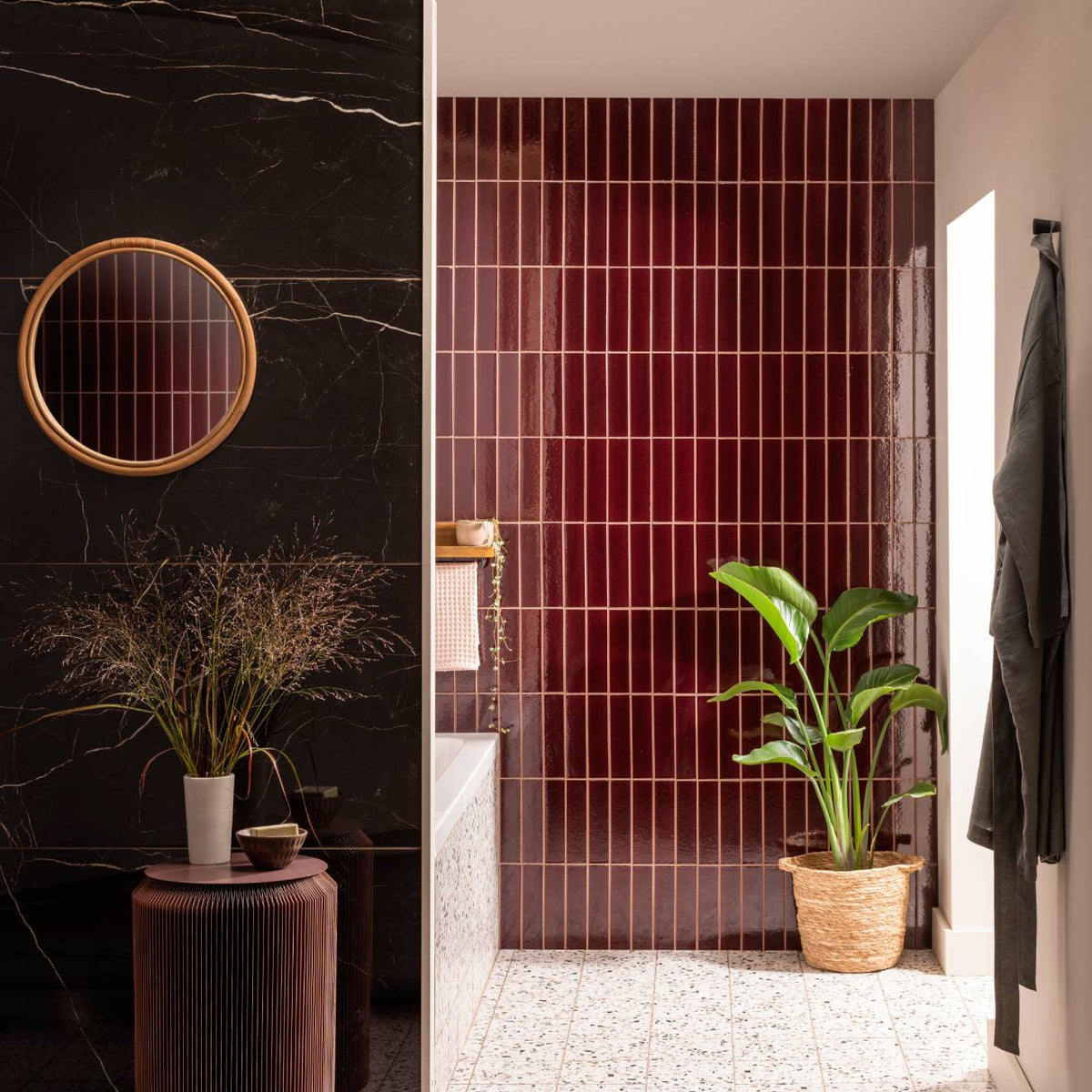 Bathroom featuring glossy black marble walls with a rattan mirror and burgundy vertical tor brick tile with a potted plant