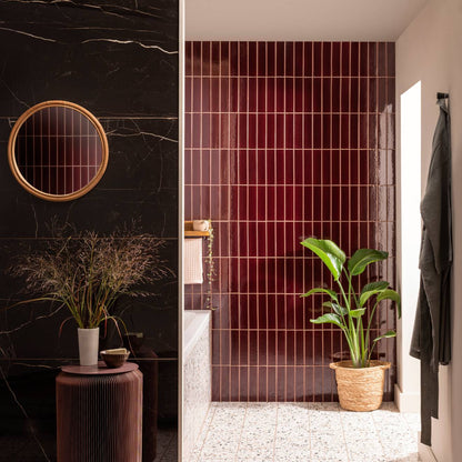 Bathroom featuring glossy black marble walls with a rattan mirror and burgundy vertical tor brick tile with a potted plant