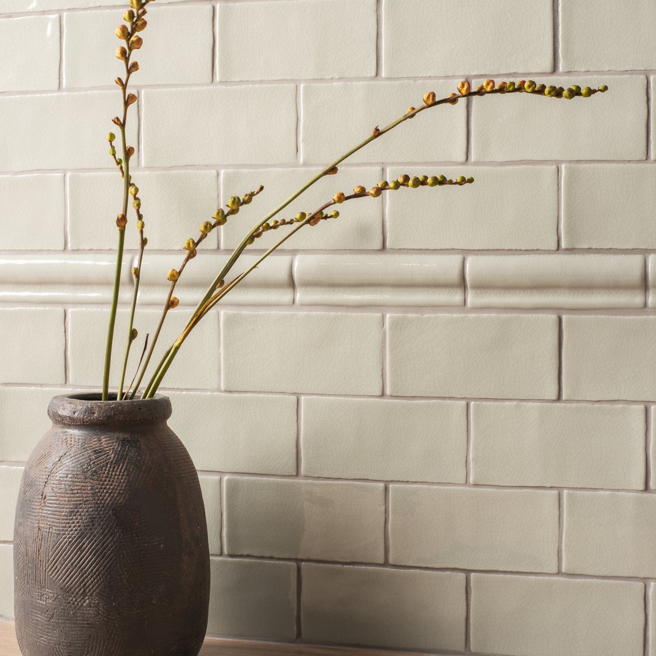 Dark gray textured ceramic vase torus moulding tern holding slender green stems with budding yellow flowers