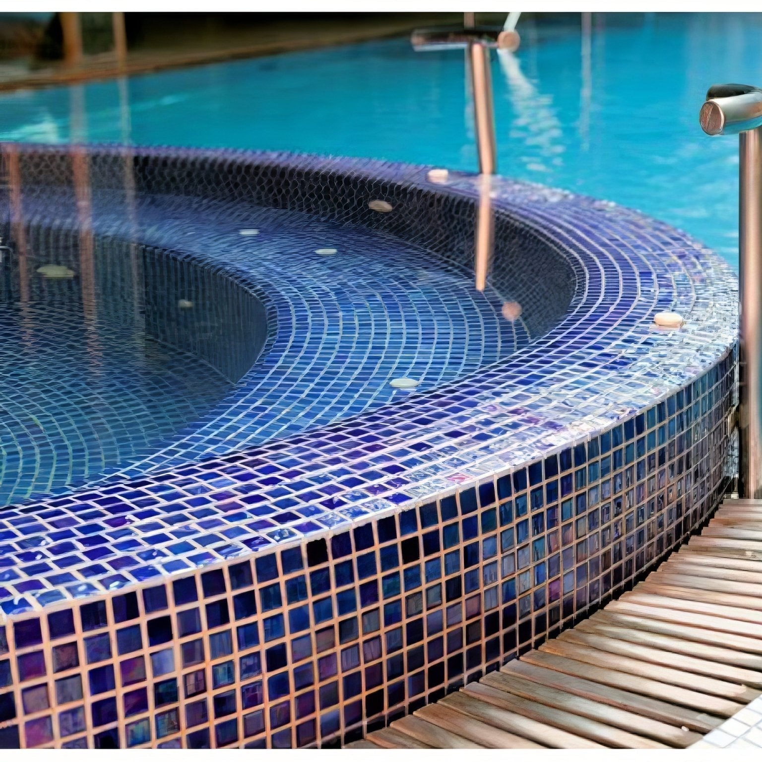 A curved hot tub lined with abalone indigo iridescent glass mosaic tiles in shades of navy to royal blue with a wooden deck