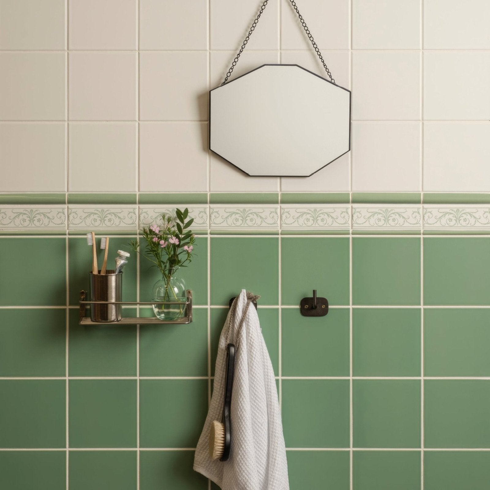 Hexagonal mirror with thin black frame hanging from chain in acanthus jade breeze on brilliant white setting