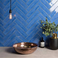 Copper-colored hammered metal vessel sink with agapanthus large brick tile background