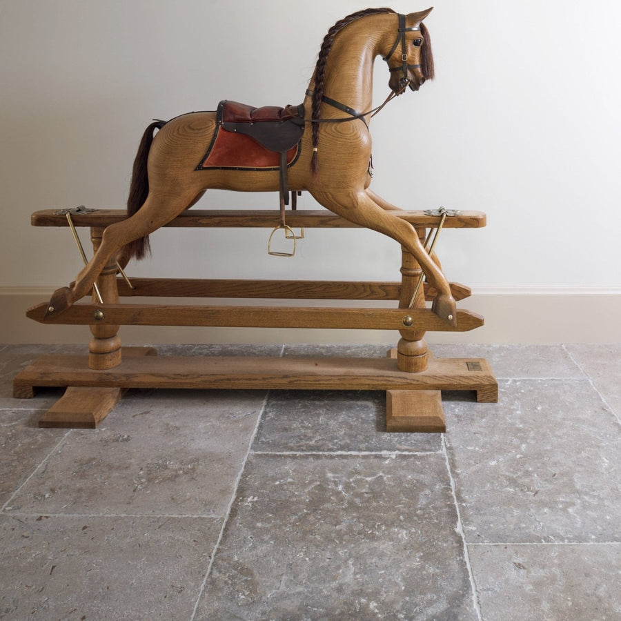 A finely crafted light brown wooden rocking horse with red and black saddle in agencourt limestone seasoned finish