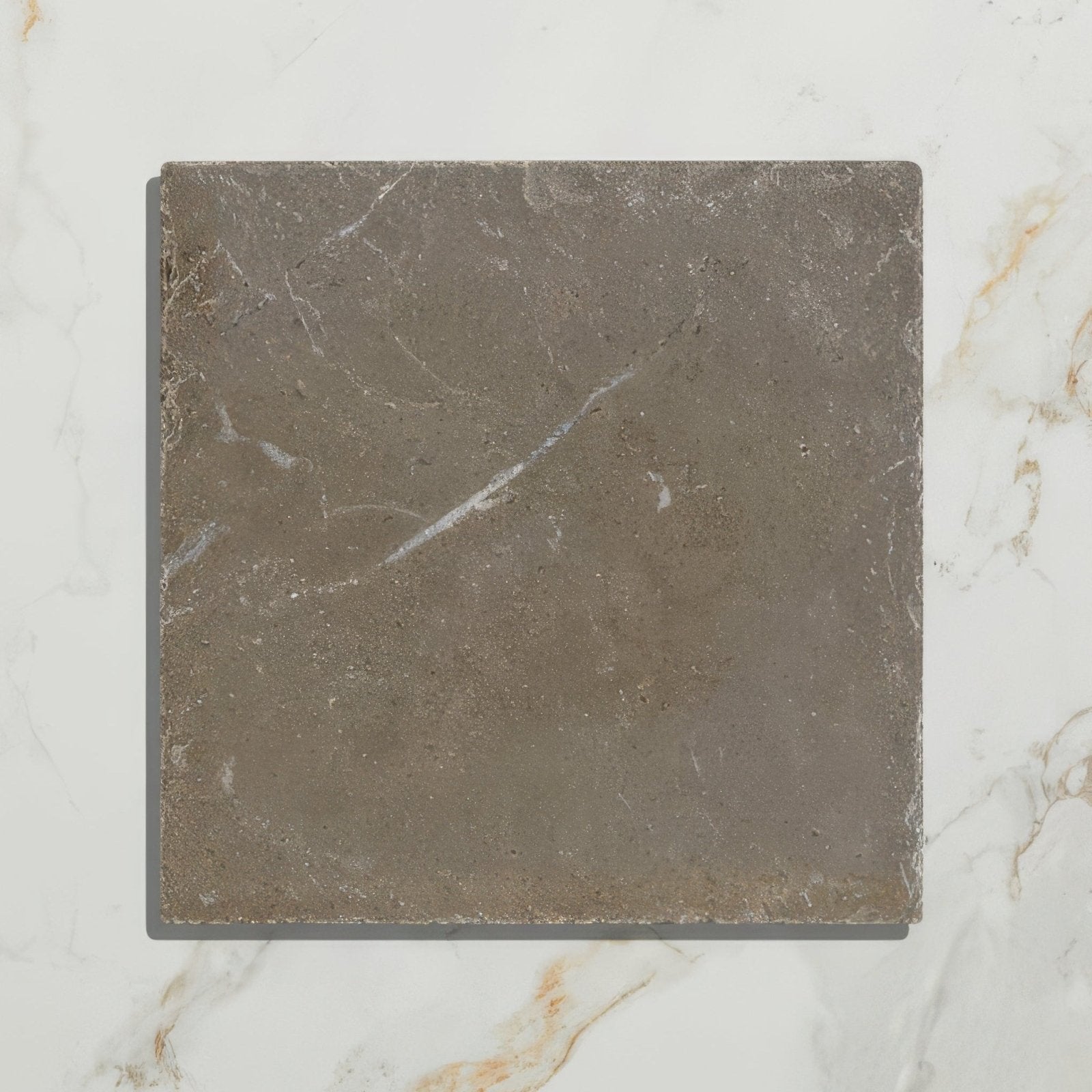 A square matte-finished gray amaya limestone tumbled cabochon tile with subtle white veining and rough texture
