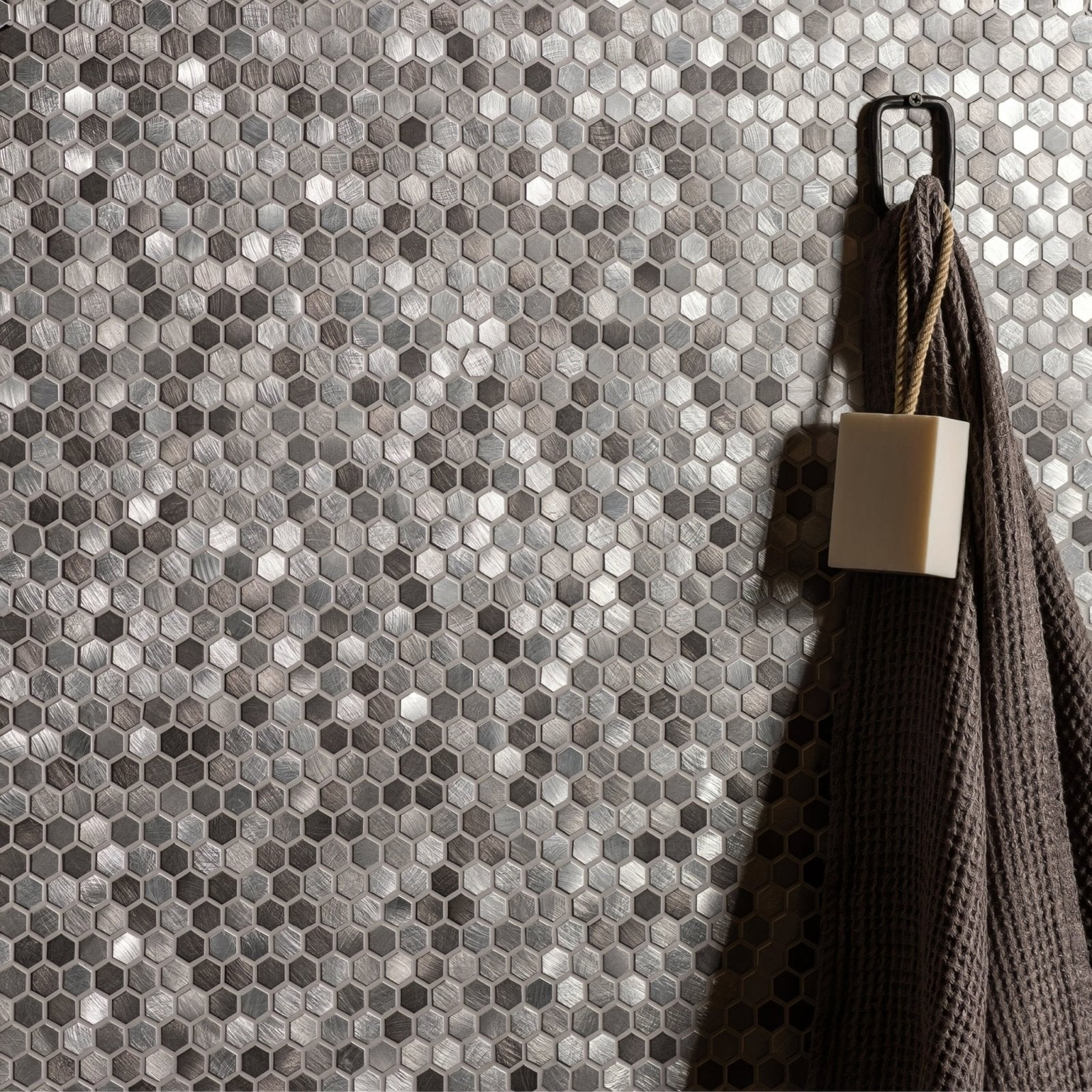 Silver hexagonal aluminium mosaic tile wall with a dark gray textured towel hanging on a black hook