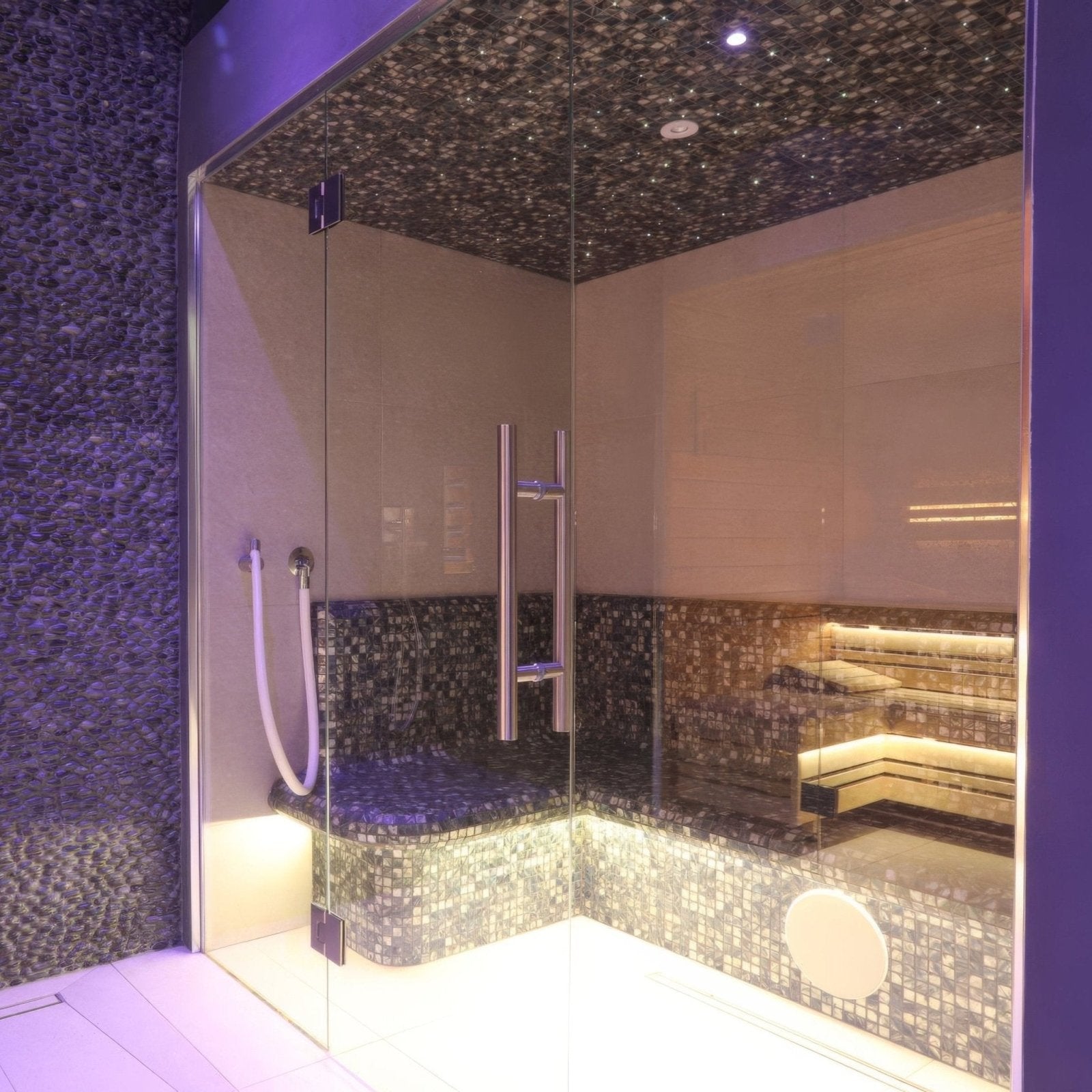 Glass-enclosed anthracite sauna with 25mm square mosaic tile walls and ceiling featuring warm underlit bench