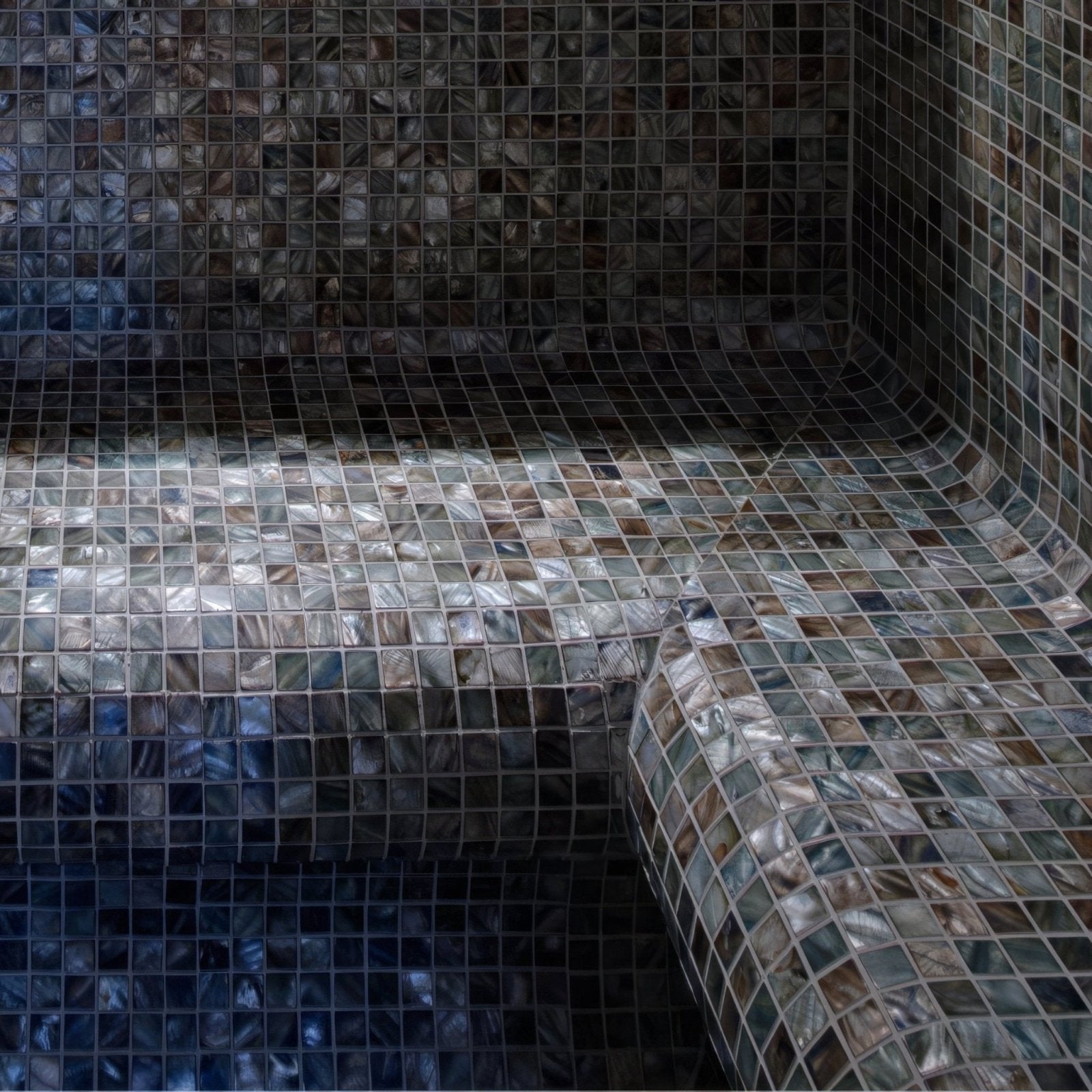 Shimmering iridescent anthracite 25mm square mosaic tiles in blue and silver forming a curved bench