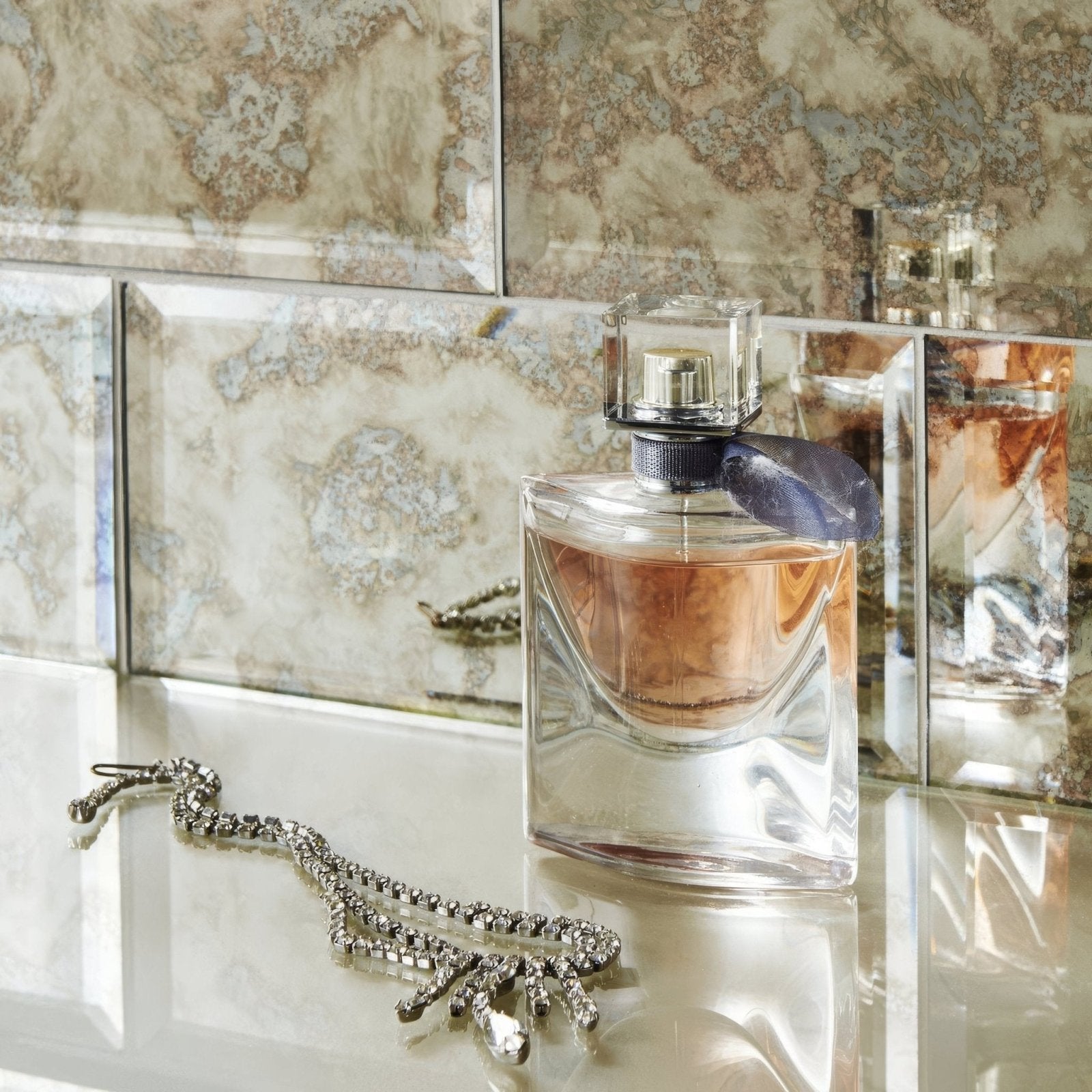 A clear glass bottle of lancôme la vie est belle perfume with silver cap and dark blue ribbon in antique mirror bevel