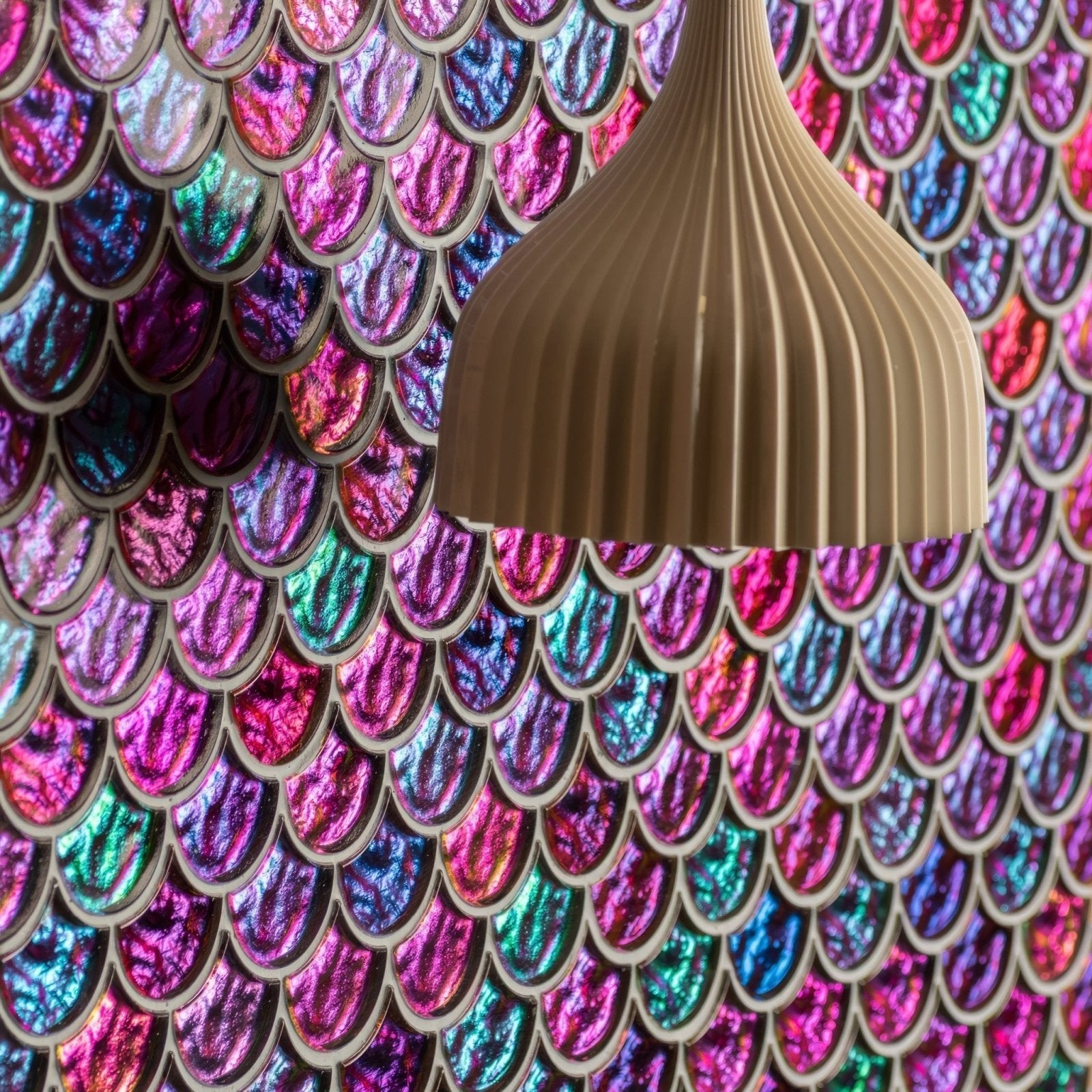 Beige ribbed pendant lamp hanging against vibrant iridescent aqua scale clear mosaic mermaid-scale wall panel