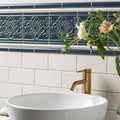 Deep blue ceramic ascot blue sigma moulding tile with raised floral patterns and white grout above subway tile backsplash