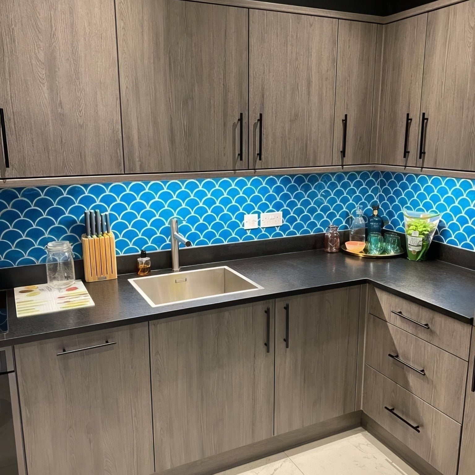 Modern stainless steel sink with a sleek rectangular design set into dark gray countertops paired with atlantis porcelain mosaic ultramarine tiles