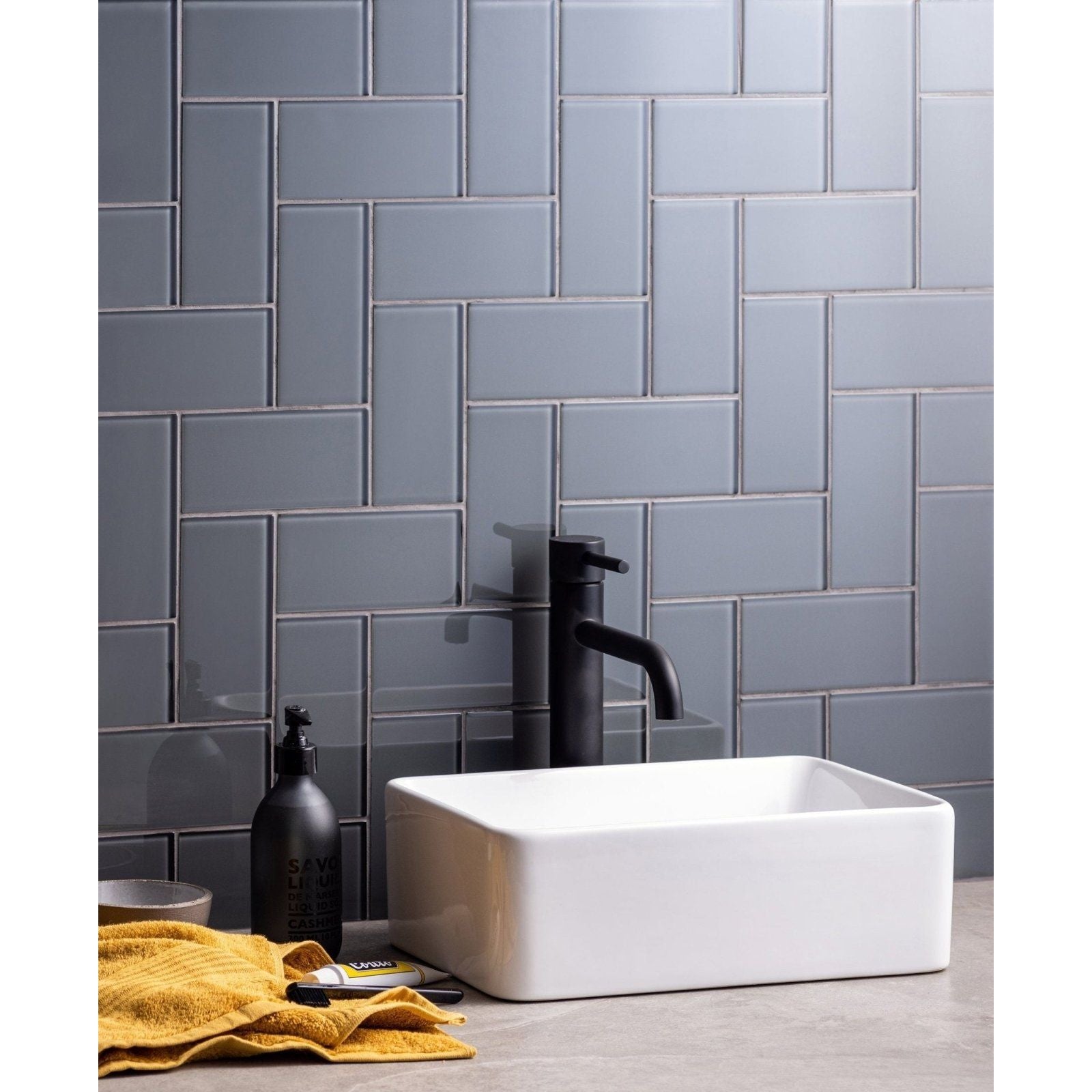 White rectangular ceramic sink with matte black faucet against gray herringbone tile backsplash featuring Avon Clear Glass Brick